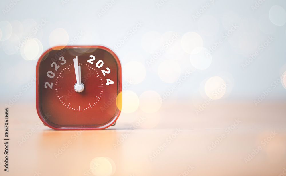 Aufkleber 2023 and 2024 on red alarm clock on wooden table with copy space and bokeh , merry christmas and hap