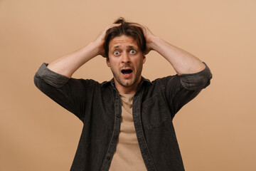 Shocked man grabbing his head isolated over beige wall