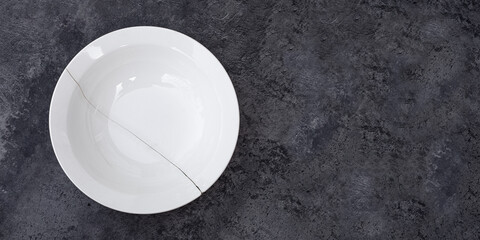 White plate with a crack in the middle on a dark surface with concrete texture, copy space
