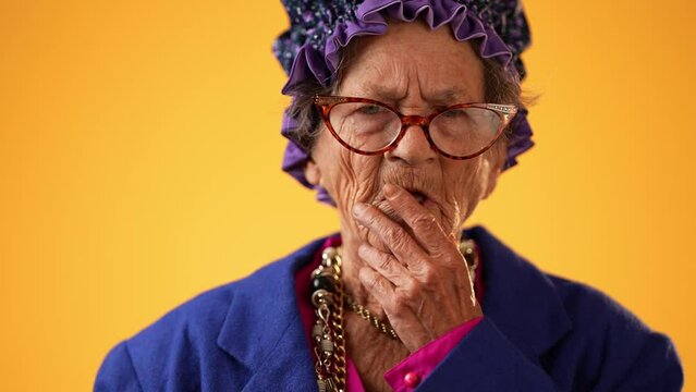 Closeup portrait of toothless funny elderly senior old woman with wrinkled skin looks at camera gives great idea gesture showing explosion of thinking posing isolated on yellow background.