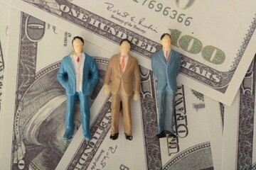 The three businessmen, a formidable trio, stood in solidarity against a money-themed backdrop,...