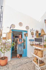  Front view of  Hispanic female owner of a small souvenir business posing proudly at the door of her business. She is looking at camera and smiling.