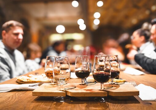 Dinner, wine tasting at old winery. Elegant wine pairing glasses filled with red, white, rose selections on rustic wooden table. Guests enjoy conversation in warm setting. Agrotourism, vineyard event