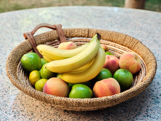 Fresh bananas in the basket with various fruits on granite garden table.