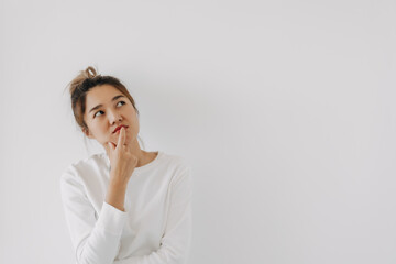 Asian Thai woman wear sweater bun hair, touching chin and mouth with doubt and curious face, have question thinking and looking at empty space, isolated on white background wall at winter. - obrazy, fototapety, plakaty