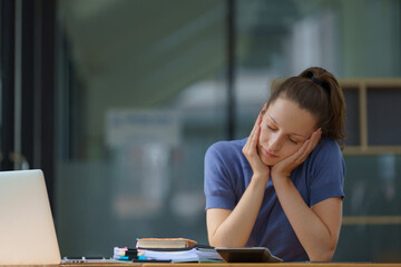 Displeased woman nearly falling asleep at work, hold her head with hand.