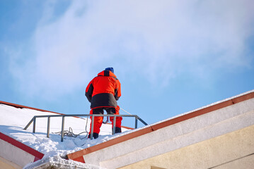 Industrial alpinist on top of the roof prepare remove snow and ice. Man on building roof, ready to remove snow and break ice and icicles on roof top. Risky work at height