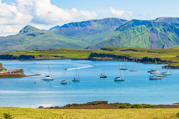 The beautiful Isle of Canna, Inner Hebrides in Summer with yachts and a catamaran in the bay and a RIB speeding towards the harbour with the Isle of Rum in the background.  Horizontal.  Copy space - obrazy, fototapety, plakaty
