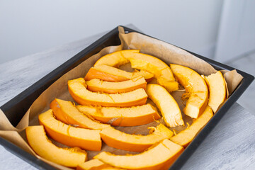 Pumpkin Slices with olive oil, herbs and salt ready for cooking in oven on a backing paper, parchment sheet on Baking Tray. Close up.