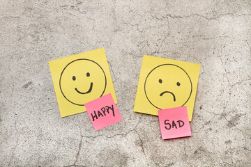 Nota adhesiva emociones de cara feliz y triste sobre un fondo gris texturado. Vista superior y de...