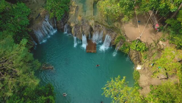 Cambugahay falls, Siquijor island, Philippines. Slow aerial travelling panning down. Cinematic drone view. Filipino tourists swimming in the turquoise waterfall. Famous travel destination.