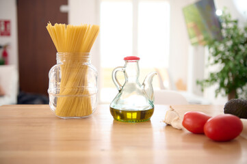 Still life. A glass oilcan of fresh extra virgin olive oil, Italian spaghetti and tomatoes on the table in home kitchen.