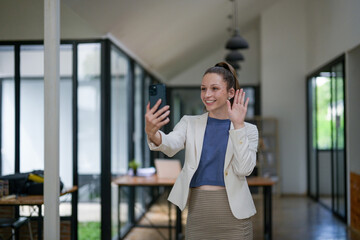 Obraz premium Smart businesswoman standing enjoying video call on phone in office. Greeting from a distance