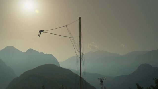 Feeling Freefall from a Mountain Against the Backdrop of a Sunset. A Tourist Spot, a Catapult Attraction. A Person Launches and Performs a Somersault in the Air.