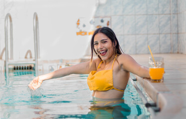 Mujer con bikini caliente atractiva sonriente sosteniendo un vaso en su mano durante un baño en la piscina , tomando sol, verano, teléfono celular,vaciones - obrazy, fototapety, plakaty