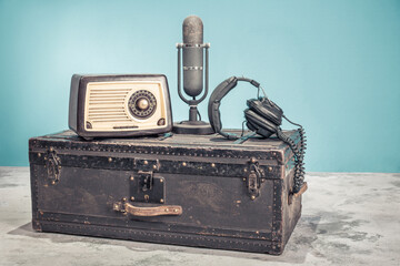 Vintage radio, classic microphone from 1950s and headphones on old aged black trunk. Retro style filtered photo