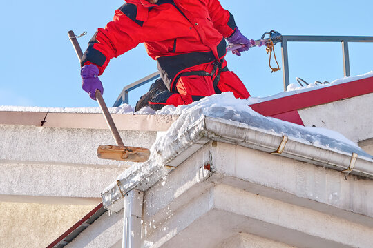 Man breaking ice, knock icicles, clean snowy rooftop. Industrial alpinist removing ice, knock down icicles from gutter and drain pipe. Preventing fall snow, ice and icicles from rooftop