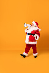 Christmas is coming ! Real Santa Claus shouting using megaphone over yellow studio background. Xmas...