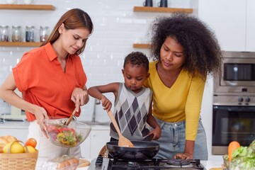 Happy Two asian women lgbtq lesbian and son making salad while preparing food in the kitchen having fun, mother and son cooking activity concept.