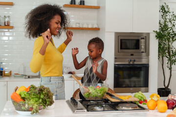 Happy African mother and son making salad while preparing food in the kitchen having fun, mother and son cooking activity concept. - obrazy, fototapety, plakaty