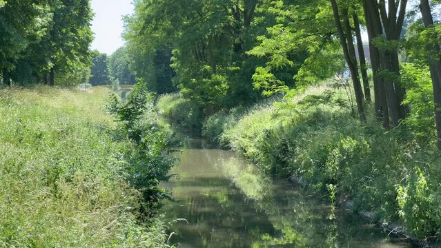Ruhiger tr&uuml;ber Fluss flie&szlig;t langsam durch ein gr&uuml;nes Idyll an einem sonnigen Tag mit gelber Br&uuml;cke im Hintergrund
