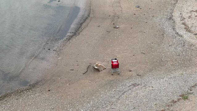 Roter verlassener Einkaufswagen und M&uuml;ll stehen in einer Bucht am Sandstrand