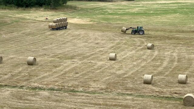 Heuballen werden von einem Frontlader Traktor auf einer weitl&auml;ufigen Wiese eingesammelt und auf einen Anh&auml;nger beladen