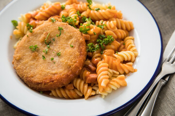 Jägerschnitzel nach DDR Rezept mit Jagdwurst paniert, Spirelli Fusilli Nudeln, Tomatensoße, Petersilie auf Emaille Teller, Besteck und grauer Leinen Serviette