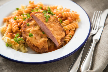 Jägerschnitzel nach DDR GDR Rezept mit Jagdwurst paniert, Spirelli Fusilli Nudeln, Tomatensoße, Petersilie auf Emaille Teller, Besteck und grauer Leinen Serviette