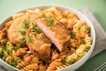 Jägerschnitzel nach DDR GDR Rezept mit Jagdwurst paniert, Spirelli Fusilli Nudeln, Tomatensoße, Petersilie auf Porzellan Schale, Besteck, beige Leinen Serviette und grünen Hintergrund
