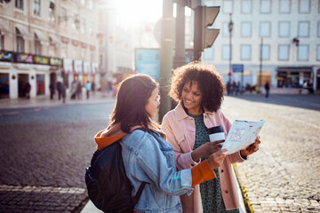 Two diverse female friends using a map to navigate the city on vacation