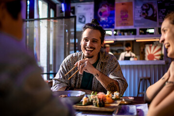 Happy young man eating sushi with his friends in a restaurant