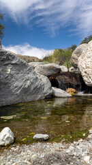 front view of a small fresh crystal water waterfall surrounded by big rocks. Taken in Merlo, San...