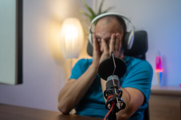 Sad person losing online video games on computer. Man playing games with headphones and controller, feeling disappointed about lost game. Player using joystick and headset at monitor. Focus microphone