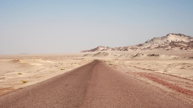 Slow driving motion by the sandy road through the wild desert. Clear blue sky and mountains on the horizon