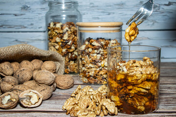 Jar full of nuts with honey removing one with a fork surrounded by whole and peeled nuts