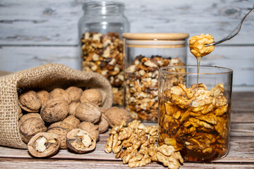 Jar full of nuts with honey removing one with a fork surrounded by whole and peeled nuts