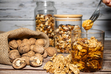 Jar full of nuts with honey removing one with a fork surrounded by whole and peeled nuts