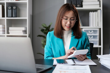 Beautiful young Asian businesswoman using laptop computer and paperworks with planning working on financial document, tax, exchange, accounting and Financial advisor