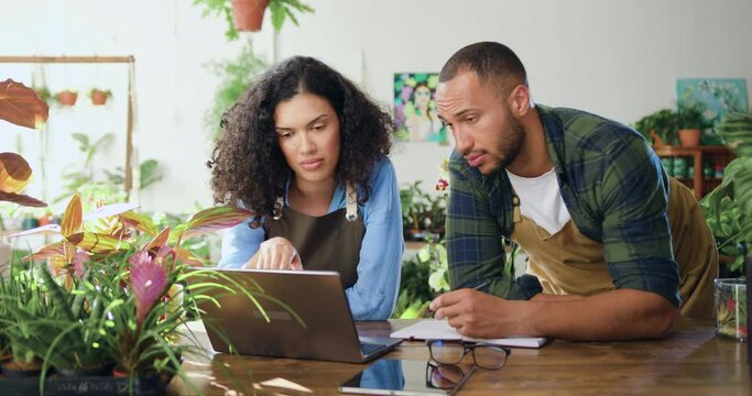 Close up portrait of african american professional florists woman and man take an order from online shop for delivery flowers sitting at desk with laptop. Family couple store owners working and doing