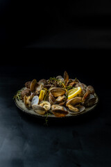 A plate of cooked vongole clams on a dark plate on a dark background.