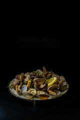 Vongole cooked with lemon and herbs on a dark background, free space, vertical photo.