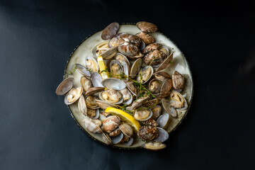 Vongole shellfish dish with lemon and herbs on a dark background, seafood appetizer. View from above. Healthy seafood.