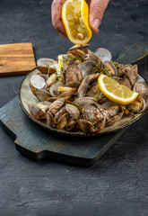 Vongole clams ready to eat are poured with lemon juice, dark background.