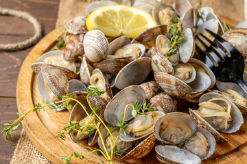 Seafood vongole clams on a wooden board, shellfish appetizer with lemon and thyme. Close-up