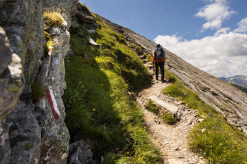 Sporty man with backpack climbing a trail uphill against the background of rocks and sky with...