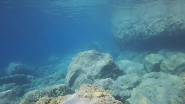 Underwater seascape with stones reef under water reflected on surface. Shallow water landscape with big stones in sun glare and surface on shallow water