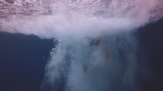 Young men jumping into deep blue sea water, underwater shot, Slow motion, Mediterranean sea. Boy dives into water and sinks to blue water in cloud of bubbles. Active male child diving underwater