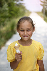 Cute laughing child little girl eats ice cream on a hot day. Ice cream in a waffle cone. A happy and contented child at summer.