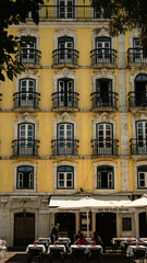 Fototapeta na wymiar Lisbon, Portugal - May 25, 2023: Facade of a yellow building with a restaurant and the esplanade on the ground floor